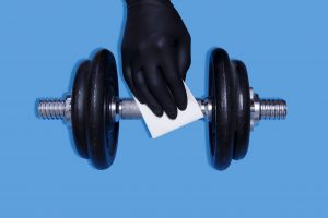 Hand in sanitary gloves cleaning dumbbells.